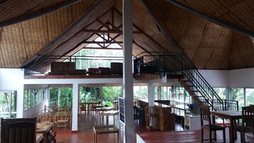 Un espacio interior amplio con techo alto, muebles de madera y una escalera que conduce a un nivel superior.
