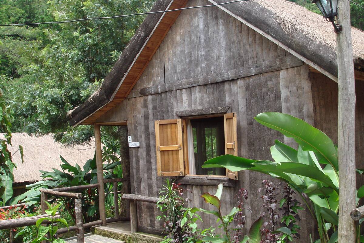 Un bâtiment rustique en bois, doté d’un toit de chaume, d’un porche en bois et d’une enseigne indiquant le numéro de la chambre : 2.