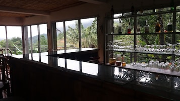 Zona de bar con vistas a exuberante vegetación y montañas a través de amplios ventanales.
