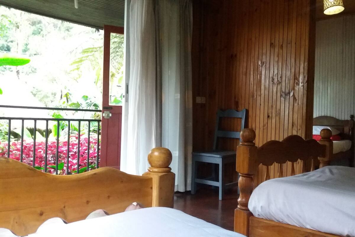 Une chambre avec deux lits en bois, une chaise et une vue sur un jardin où poussent des fleurs roses.