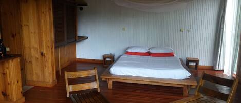 Habitación de cabaña de madera con una cama, dos sillas de madera, una pequeña mesa y un banco de madera.