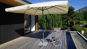 A wooden deck with a white umbrella, a chair, and a car parked in the background. - VILLA OSSATURE NEW WOOD WITH SWIMMING POOL in residential area (Saint-Jorioz)