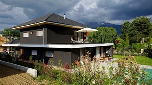 A modern two-story house with a balcony, a pool, and a mountainous backdrop. - VILLA OSSATURE NEW WOOD WITH SWIMMING POOL in residential area (Saint-Jorioz)