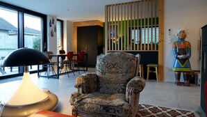 A modern living room with a large armchair, a dining area, and a decorative statue. - VILLA OSSATURE NEW WOOD WITH SWIMMING POOL in residential area (Saint-Jorioz)