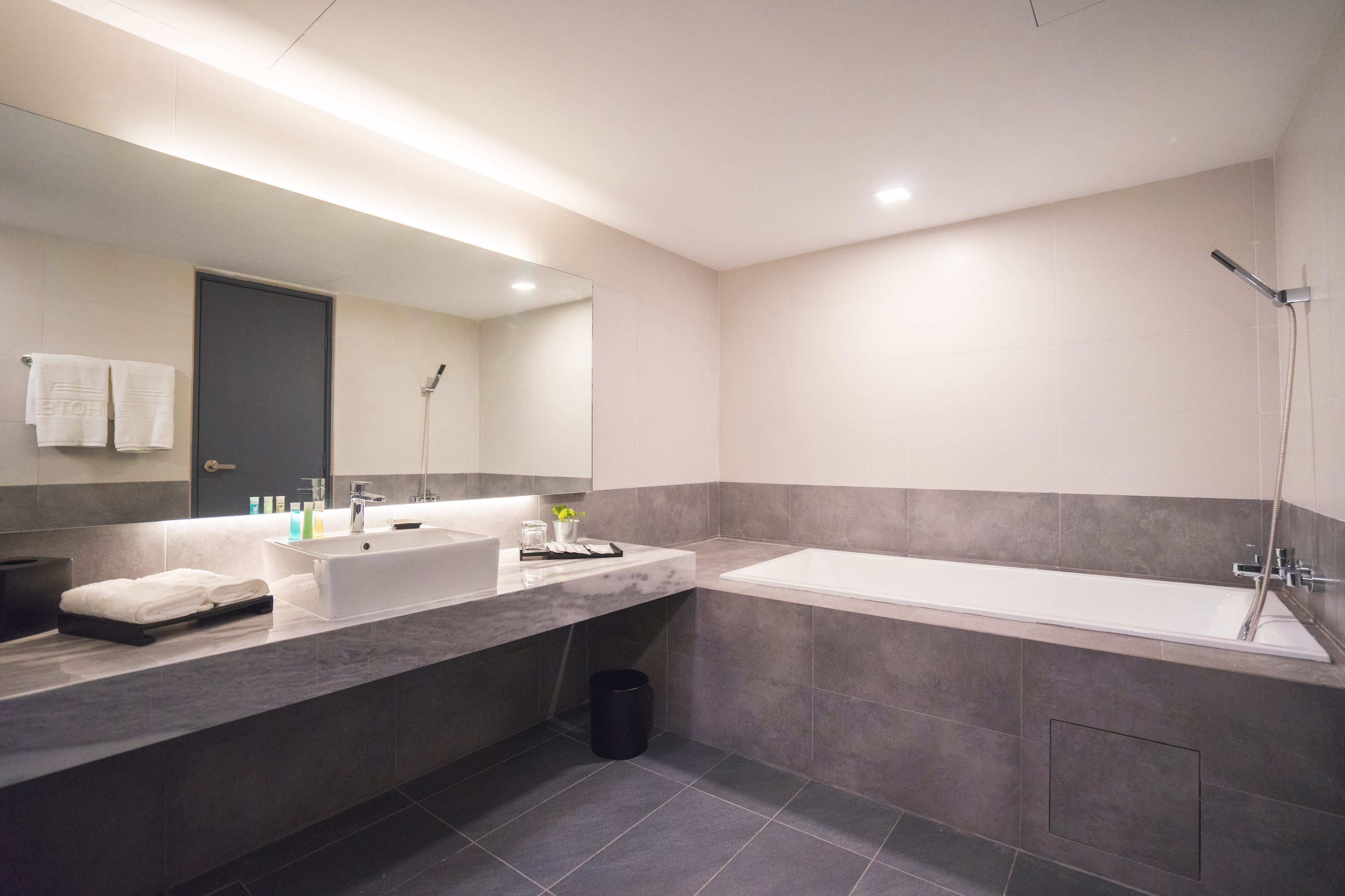 A modern bathroom with a large mirror, two sinks, a bathtub, and a shower.