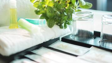 A neatly arranged bathroom with a white towel, a green plant, a bottle of liquid soap, and a glass of water on a black tray.