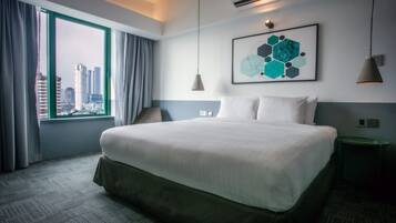 A hotel room with a large bed, a view of the cityscape, a modern art piece on the wall, and a green side table.