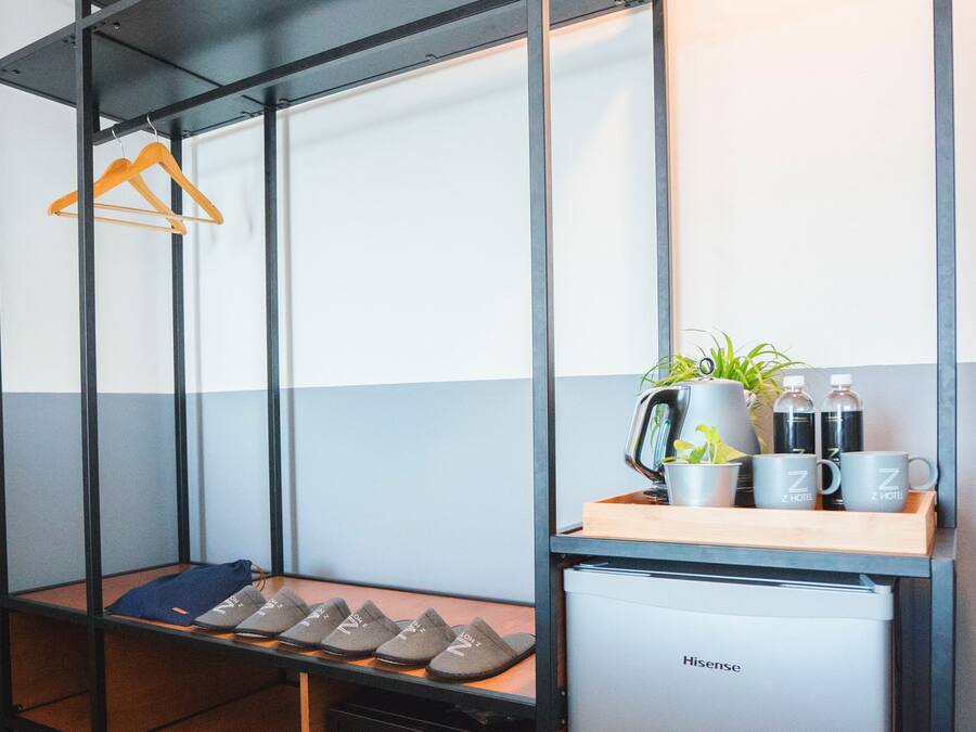 Una habitación de hotel compacta con una cama de estructura metálica, una pequeña kitchenette y un área de descanso con una mesita.