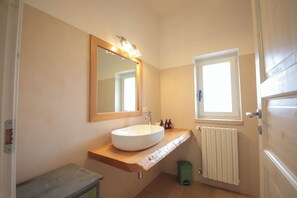 Une salle de bain avec un meuble-lavabo en bois, un lavabo blanc, un miroir, une fenêtre et un radiateur.