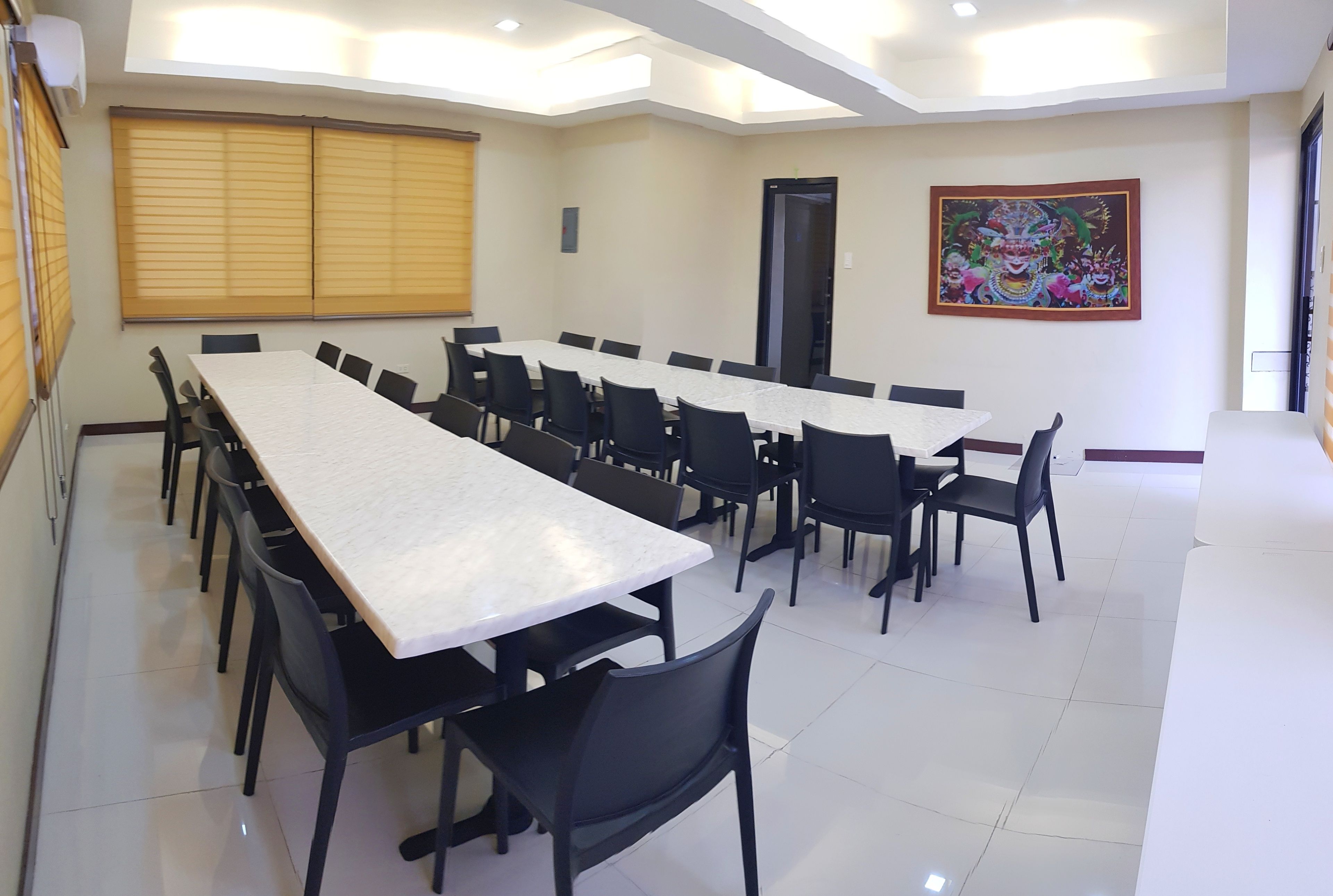 Un salón de conferencias con una larga mesa y sillas, una puerta y un cuadro colorido en la pared.
