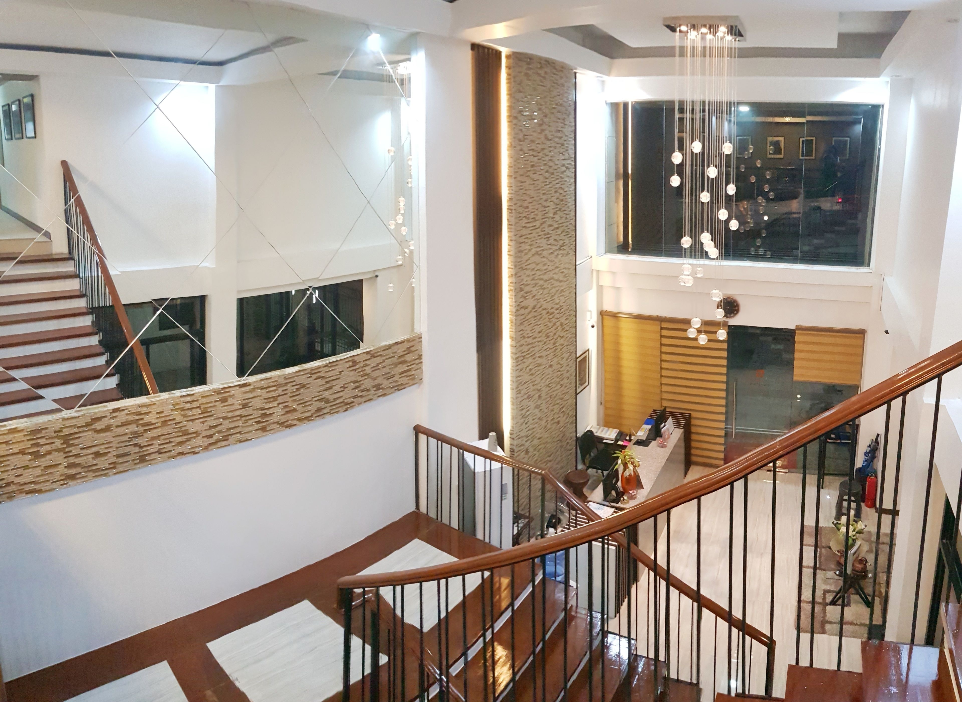 A modern interior with a wooden staircase, a reception desk, and a view of the upper floor.