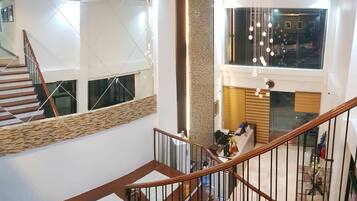 A modern interior with a wooden staircase, a reception desk, and a view of the upper floor.
