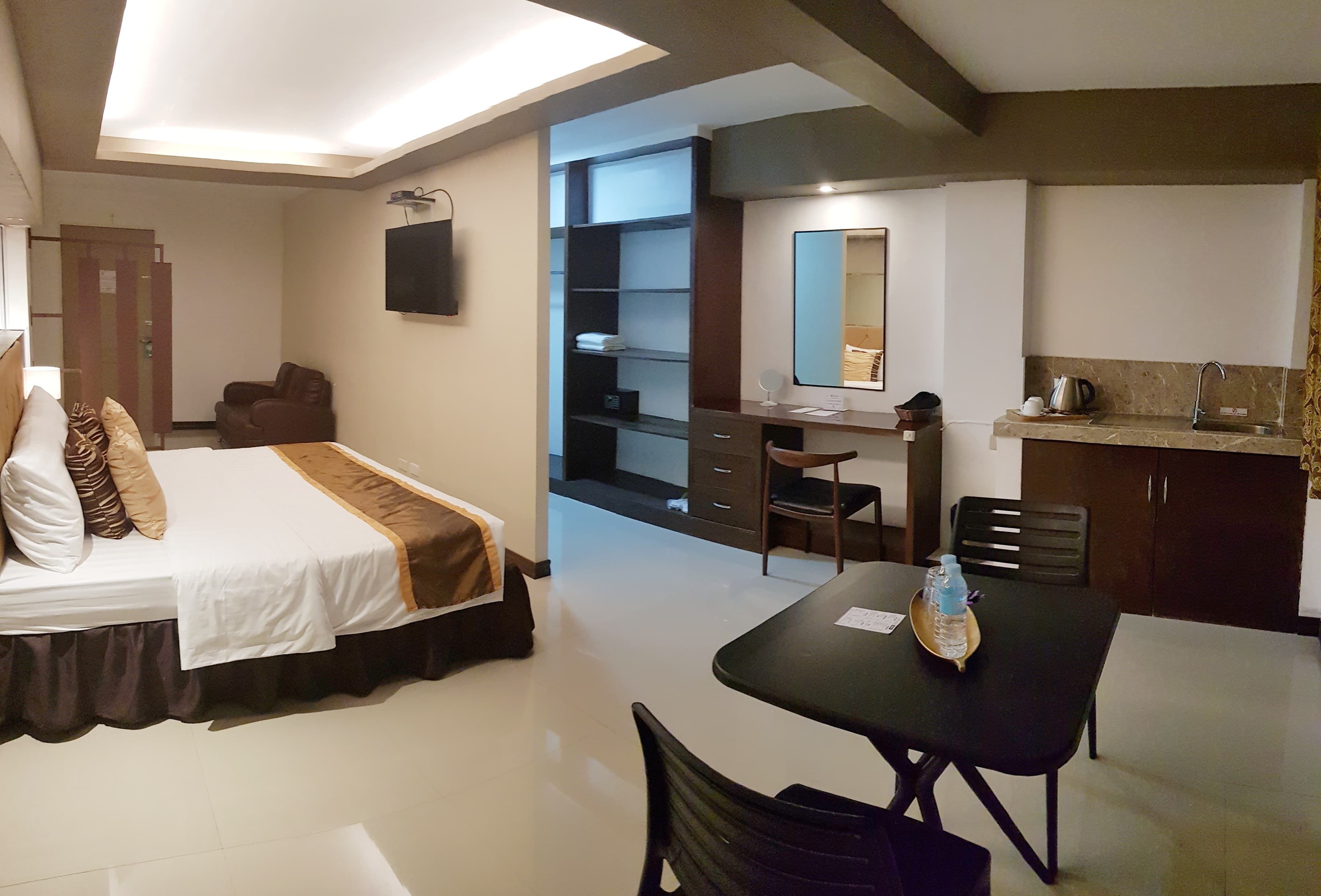 Una habitación de hotel con cama, escritorio, mesa de comedor y kitchenette.