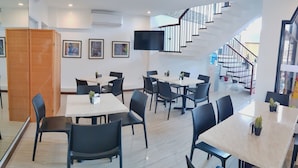 A modern dining area with multiple tables and chairs, a wooden cabinet, and a staircase leading to an upper level. - North Tourist Inn (Bacolod)