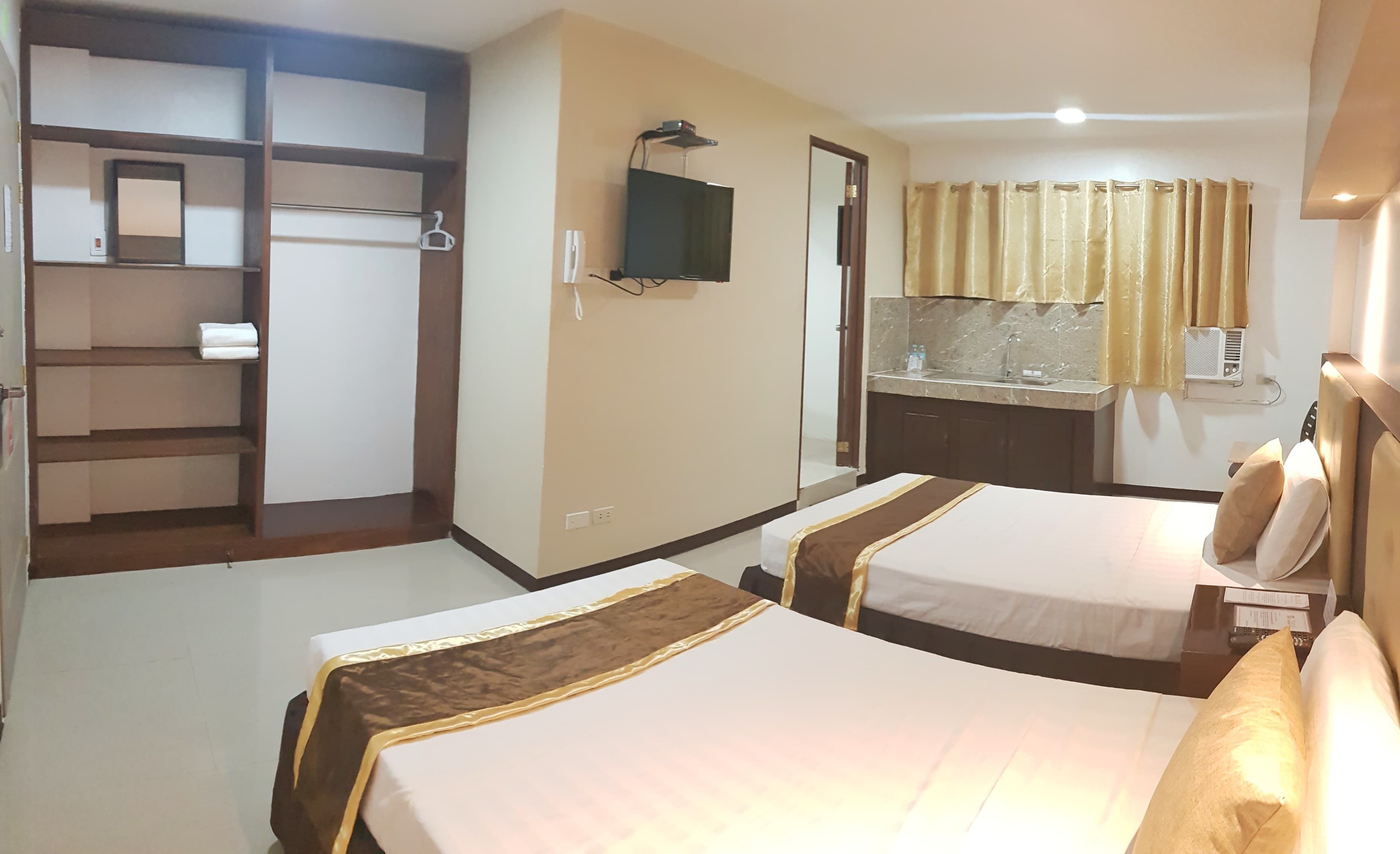 A hotel room with two beds, a TV mounted on the wall, a bathroom with a sink and mirror, and a wardrobe with a mirror.
