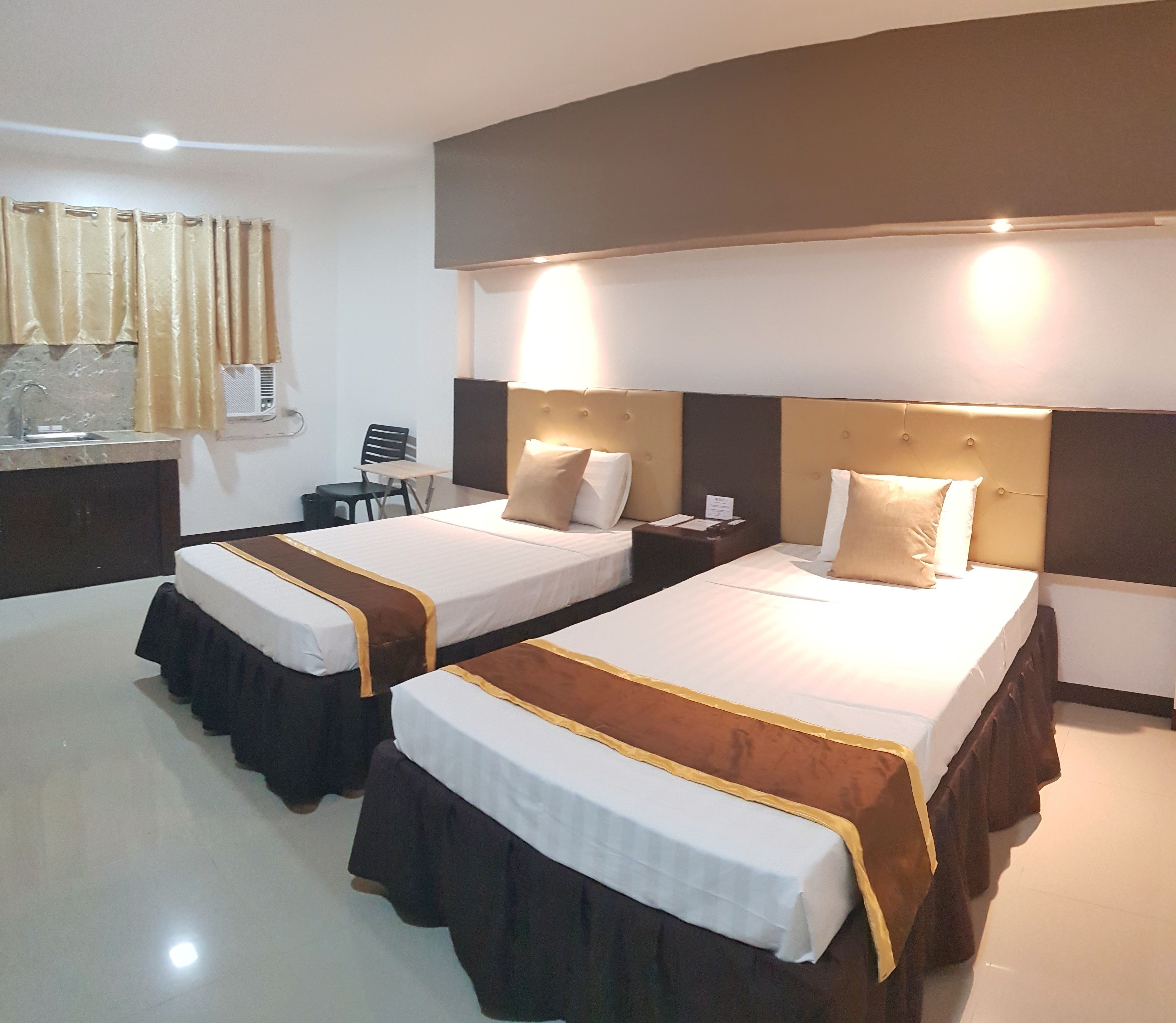 A hotel room with two beds, a desk, a chair, and a window with curtains.