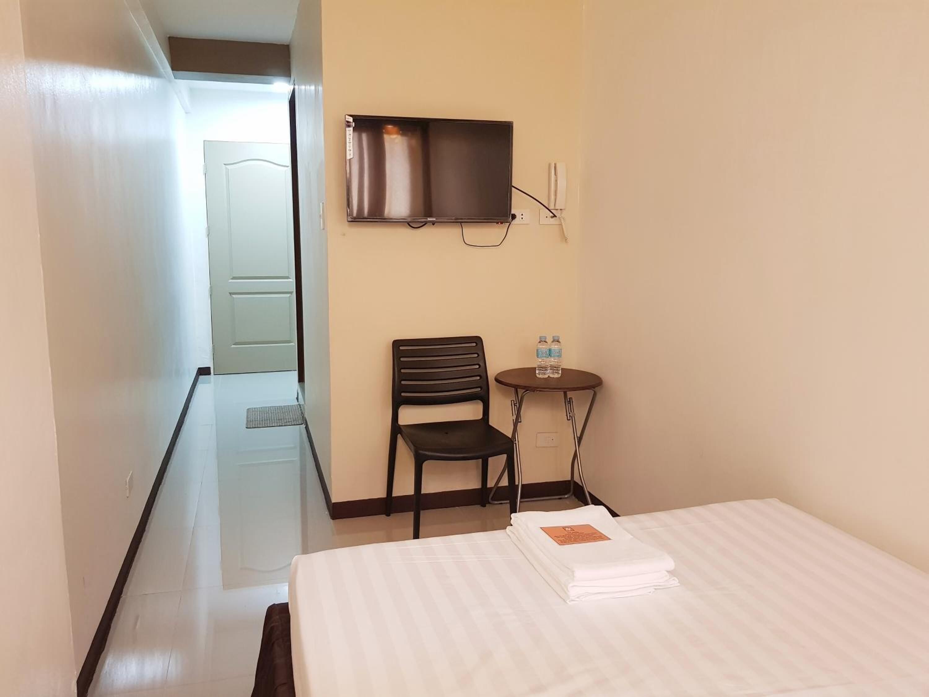 Una habitación de hotel con cama, una silla, una mesita con botellas de agua y un televisor en la pared.