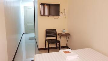 Una habitación de hotel con cama, una silla, una mesita con botellas de agua y un televisor en la pared.