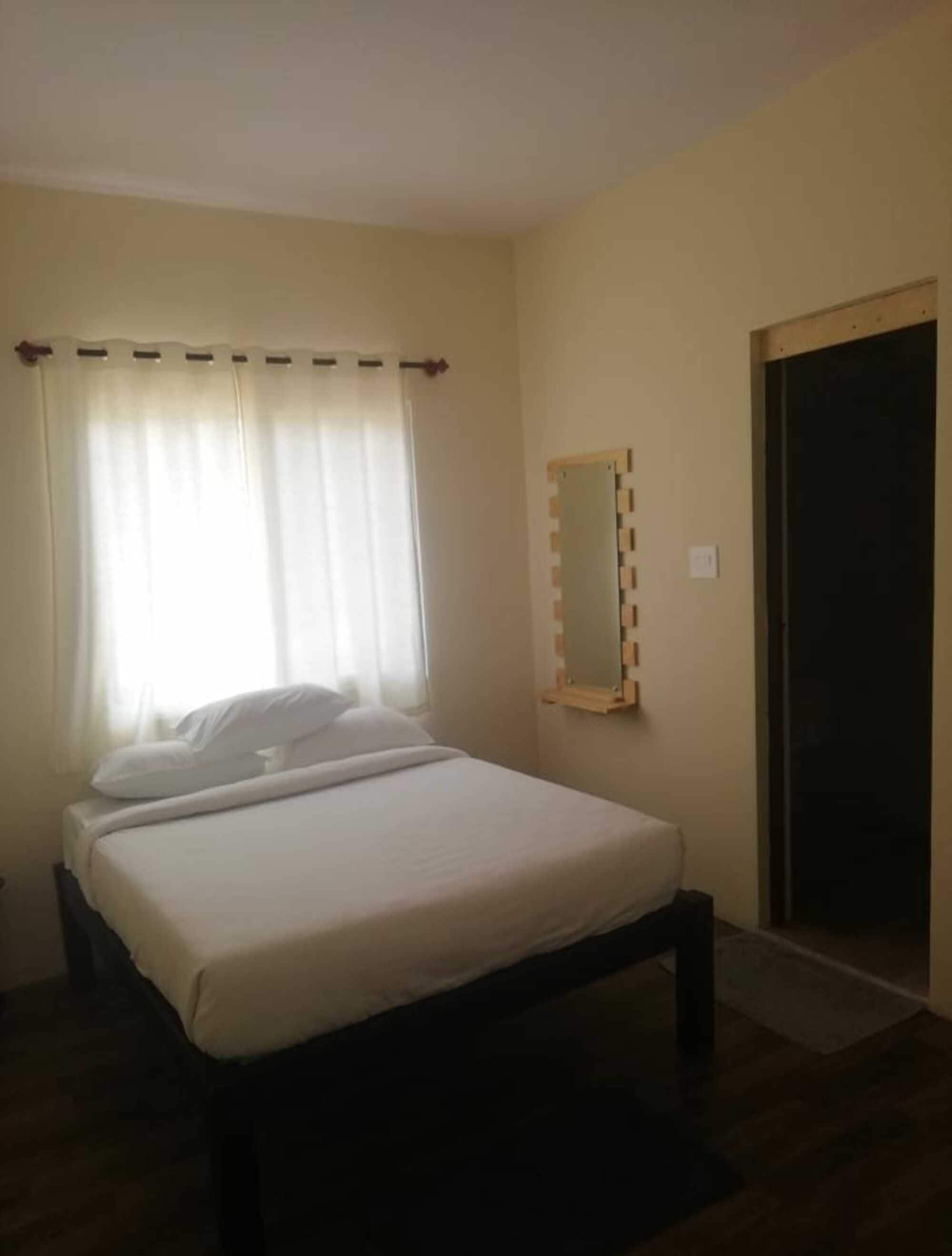 Una camera da letto con un letto, una finestra con tende, uno specchio e una porta.