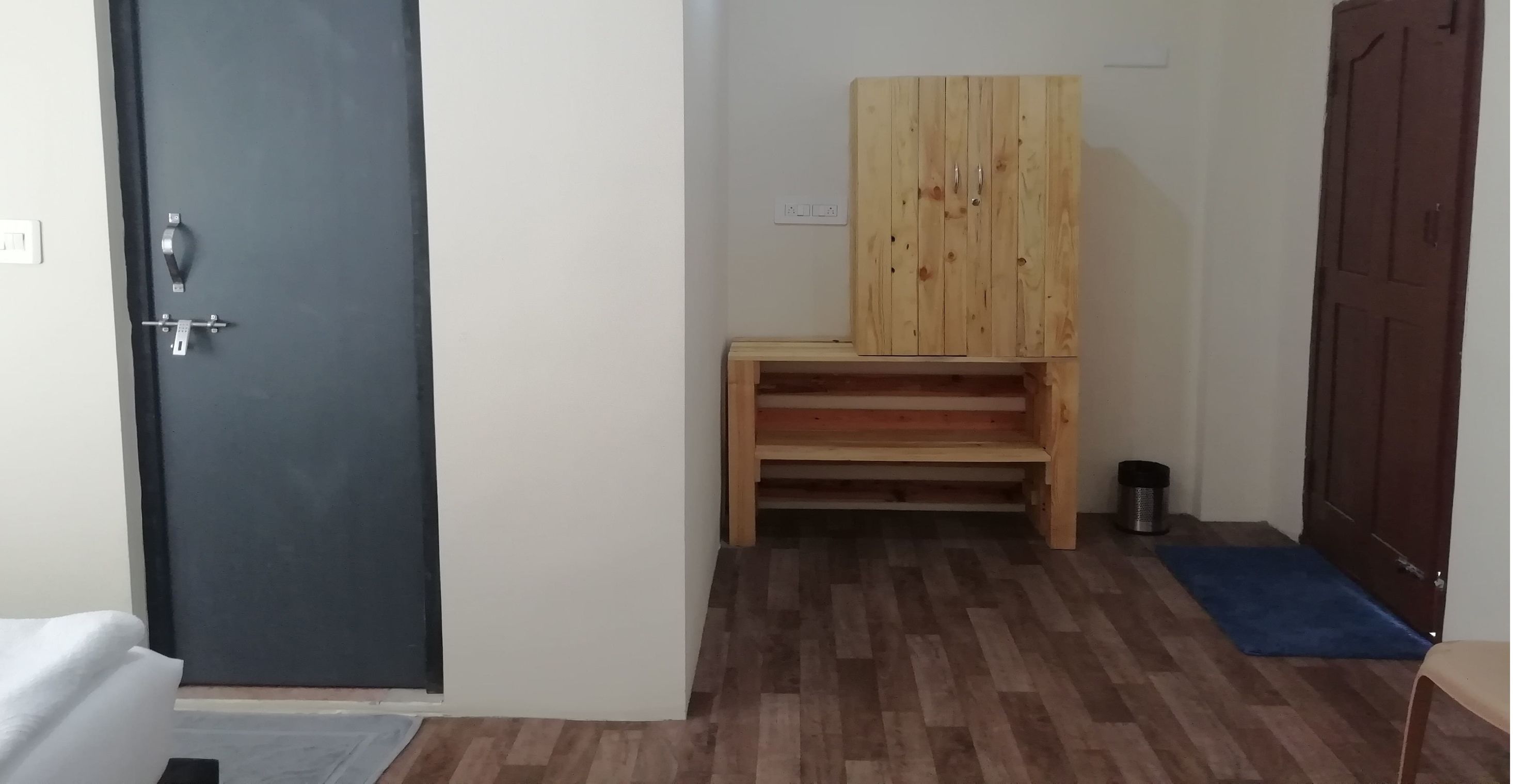 A room with a dark door, a wooden cabinet, a bench, a trash bin, and a blue mat.
