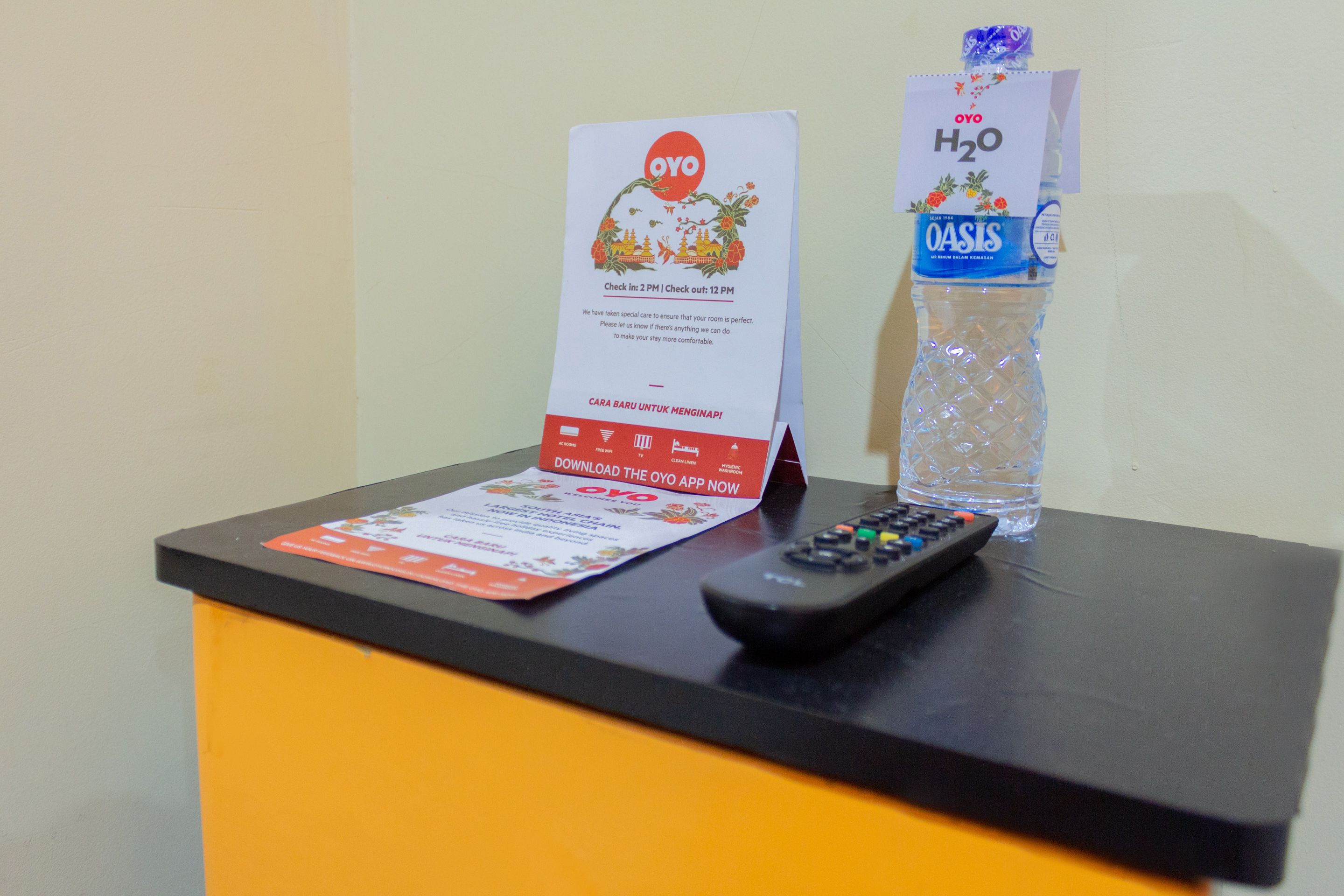 Taulell de recepció d'hotel amb un comandament a distància, una ampolla d'aigua i una targeta promocional de l'aplicació OYO.