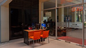 A hotel reception area with a glass door, a reception desk, and orange chairs. - Capital O 989 Audah Guesthouse Syariah (Jakarta)