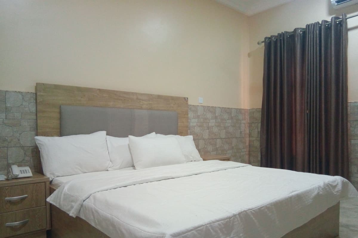 A neatly made bed with white linens, a wooden headboard, and a stone accent wall.