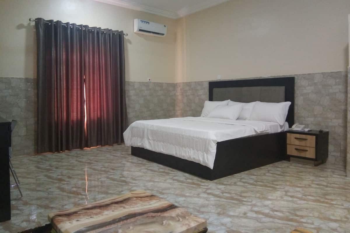 A bedroom with a bed, a nightstand, a telephone, and an air conditioning unit.