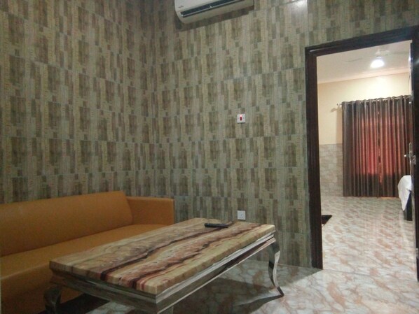 A room with a patterned wallpaper, a sofa, a table with a marble-like top, and an air conditioning unit. - Suncourt Feel At Home Suites (Abuja)