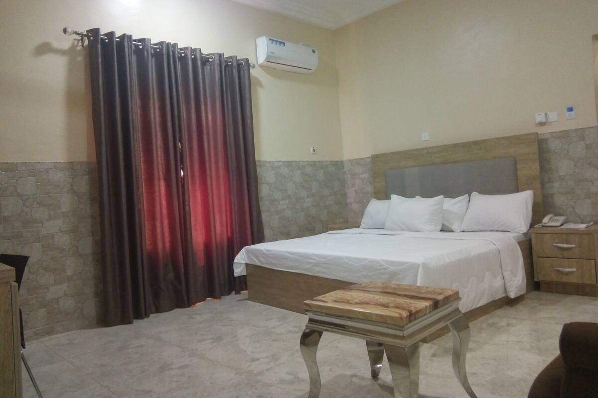 A hotel room with a bed, bedside table, and a curtain.
