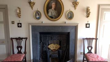 A room with a fireplace, two chairs, and a portrait above the fireplace.