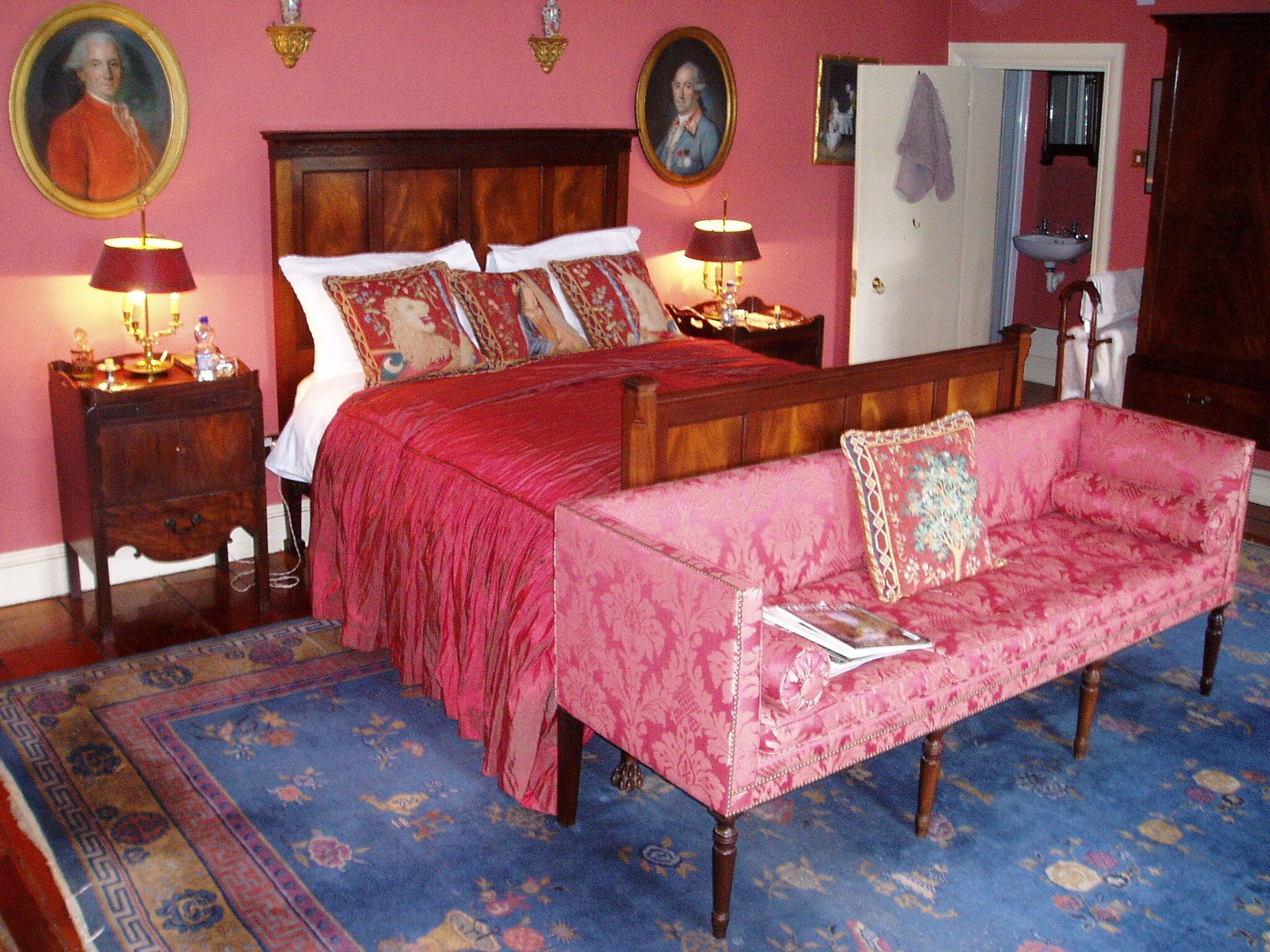 A bedroom with a large bed, a sofa, two bedside tables with lamps, and a wardrobe.