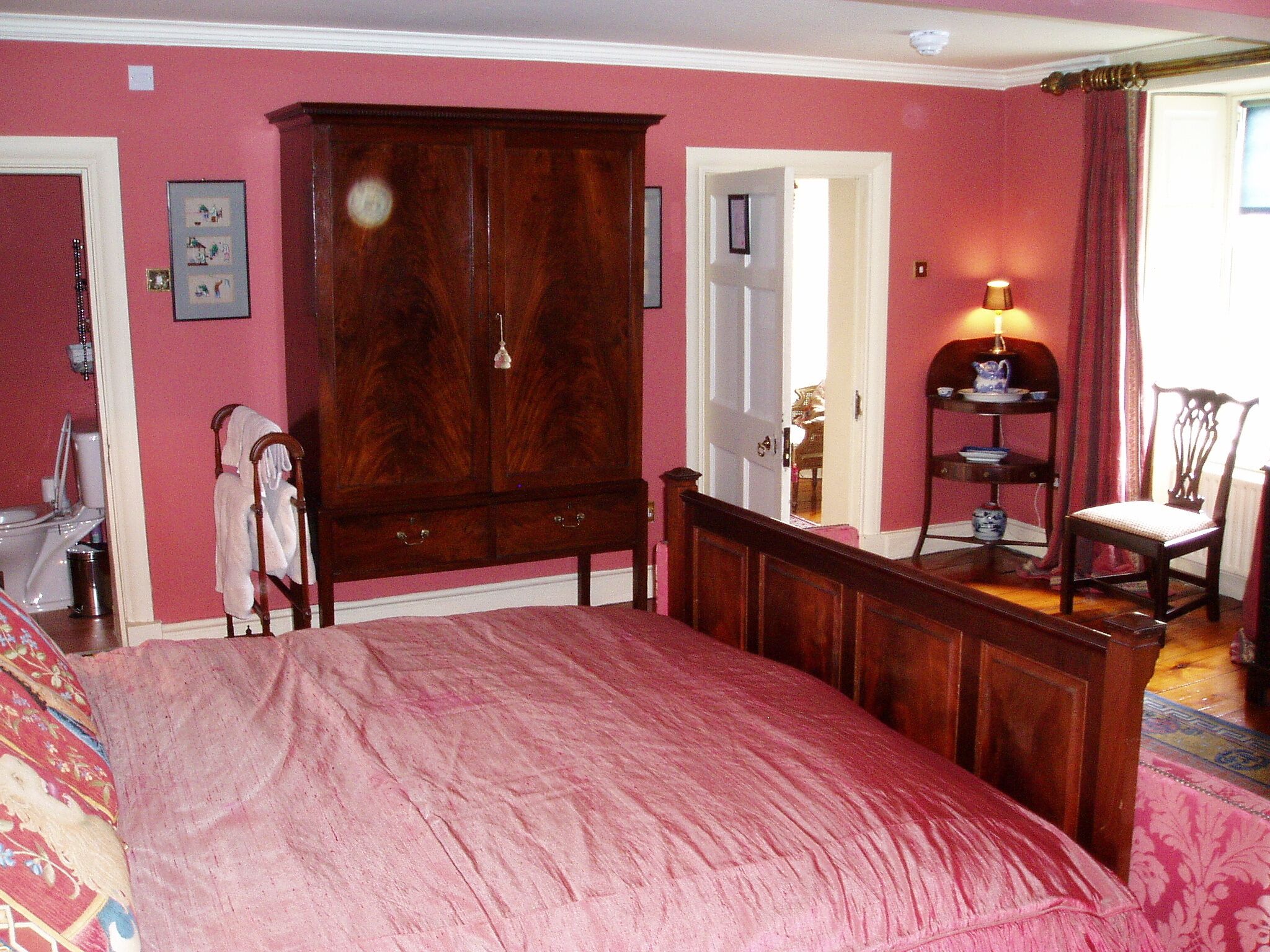 Un dormitorio con una cama grande, un armario de madera, una silla y una mesita de noche con una lámpara.