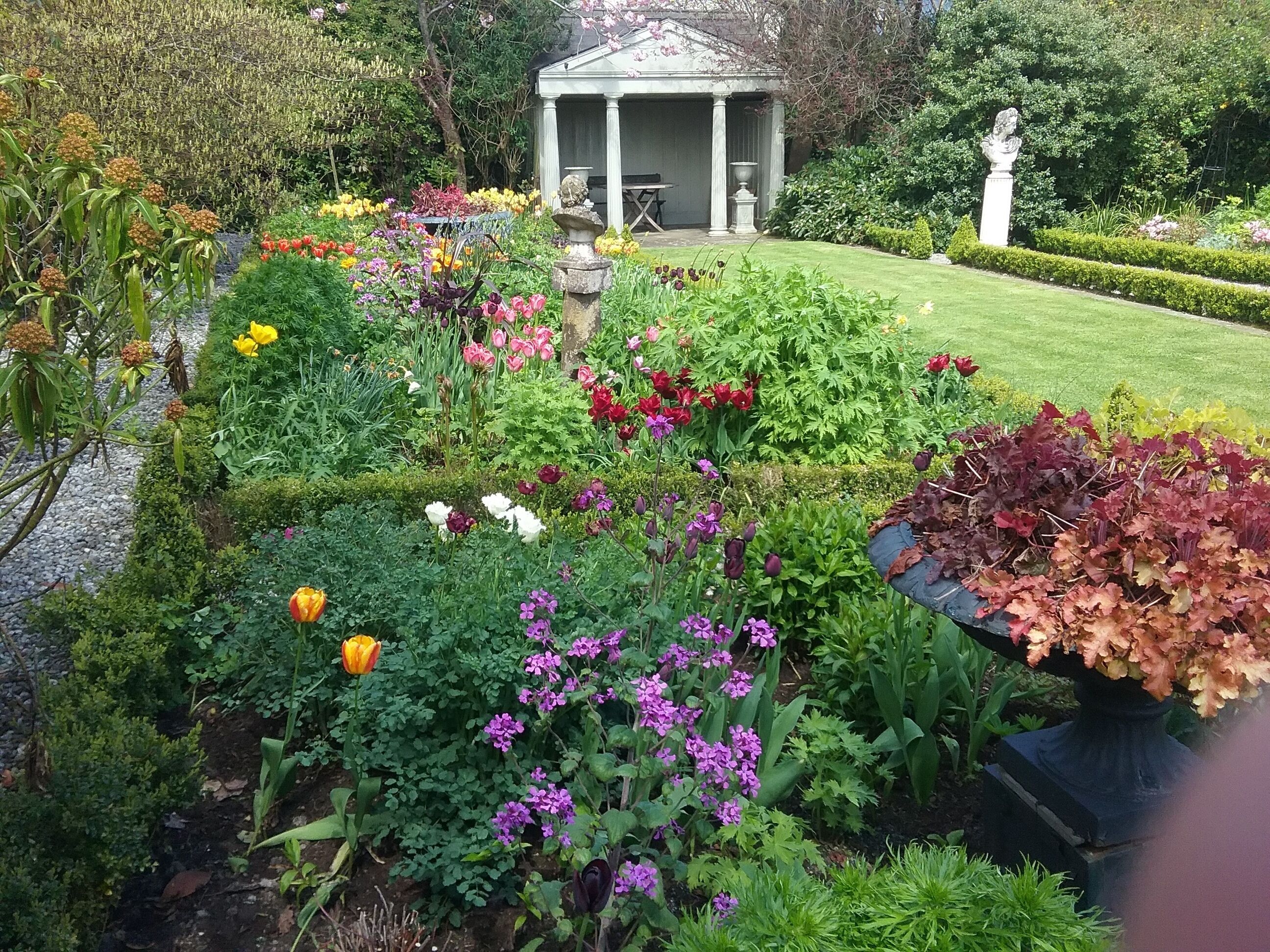 Ein Garten mit einem Pavillon, verschiedenen Blumen und einer Statue.