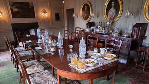 A formal dining room with a long wooden table set for a meal, surrounded by chairs with patterned upholstery.