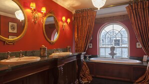 A bathroom with two sinks, a large mirror, wall sconces, and a window with a view of a building.