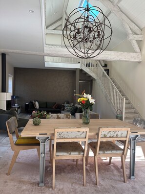 A dining area with a wooden table and chairs, a chandelier, and a staircase leading to an upper level. - Une Odeur de Tilleul (Montbrison)