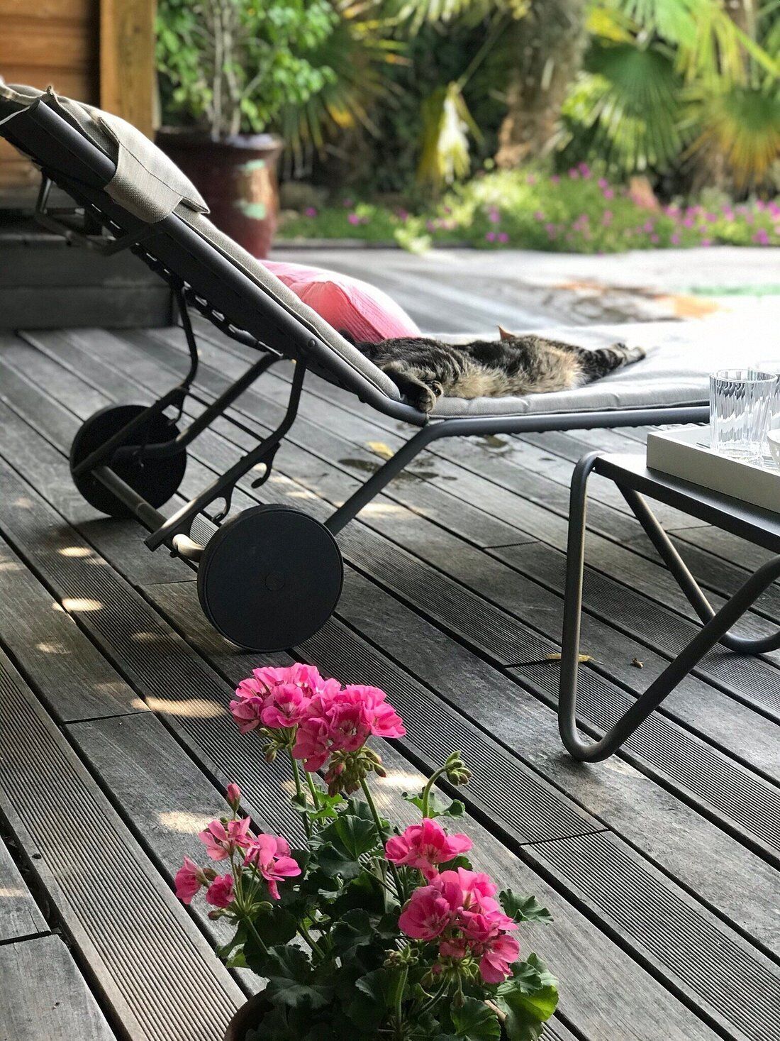A wooden deck with a lounge chair, a small table, and pink flowers.