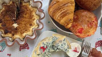 Ein Frühstückstisch mit Quiche, Croissants, Käse und Schinken, gedeckt mit einer bunten Tischdecke.