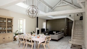 A spacious dining area with a high ceiling and exposed beams, a cozy living room with a sofa and television, and a staircase leading to an upper level. - Une Odeur de Tilleul (Montbrison)