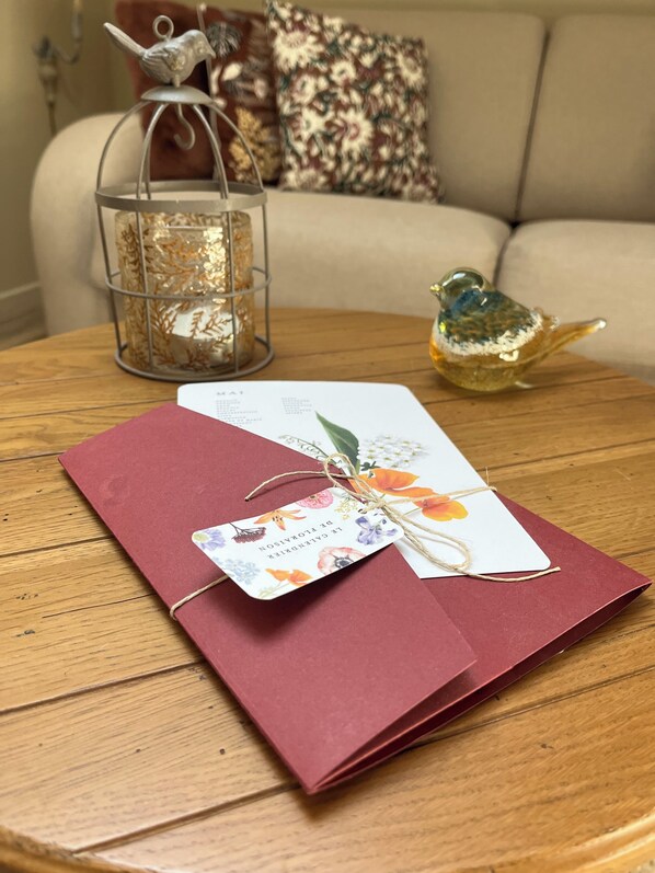 A wooden table with a red folder, a decorative bird, and a glass candle holder. - Une Odeur de Tilleul (Montbrison)