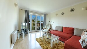 A modern living room with a red sofa, a glass coffee table, and a TV on a stand. - Select Serviced Accommodation - Hunters Wharf (Reading)