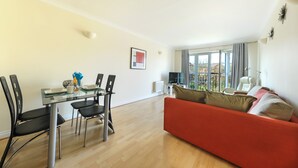 A modern living room with a glass dining table, black chairs, a red sofa, and a large window with curtains. - Select Serviced Accommodation - Hunters Wharf (Reading)