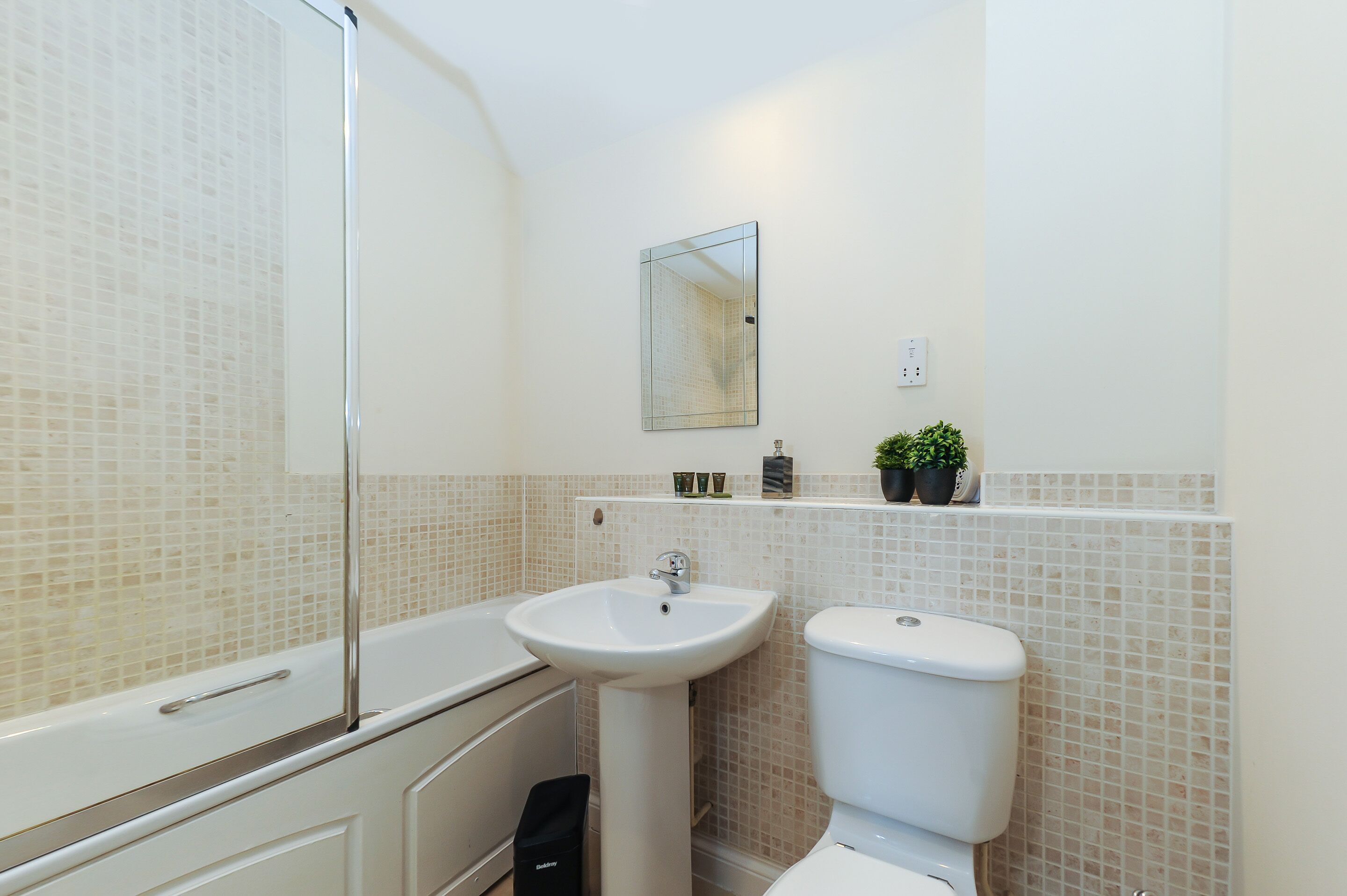 A bathroom with a bathtub, sink, and toilet. There is a mirror above the sink and a shelf with toiletries.
