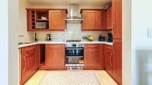A compact kitchen with wooden cabinets, a microwave, a gas stove, and an oven. - Select Serviced Accommodation - Hunters Wharf (Reading)