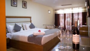 A hotel room with a neatly made bed, a bottle of wine, and two glasses on a table. - Hotel Shobla Royale (Kullu)