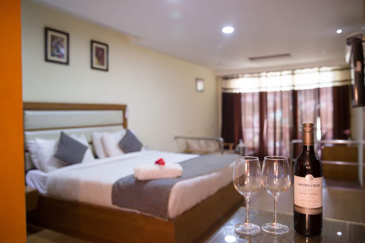 Habitación de hotel con una cama bien hecha, una botella de vino y dos copas sobre una mesa.