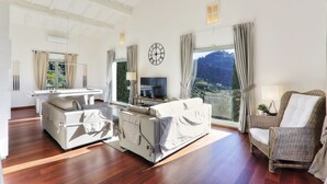 A spacious living room with a sofa, armchair, and a TV on a stand.