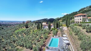 A villa with a swimming pool, surrounded by olive trees and a view of the city.