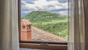 Una ventana con cortinas, vista a una colina verde con un edificio en la cima, y un cielo despejado.